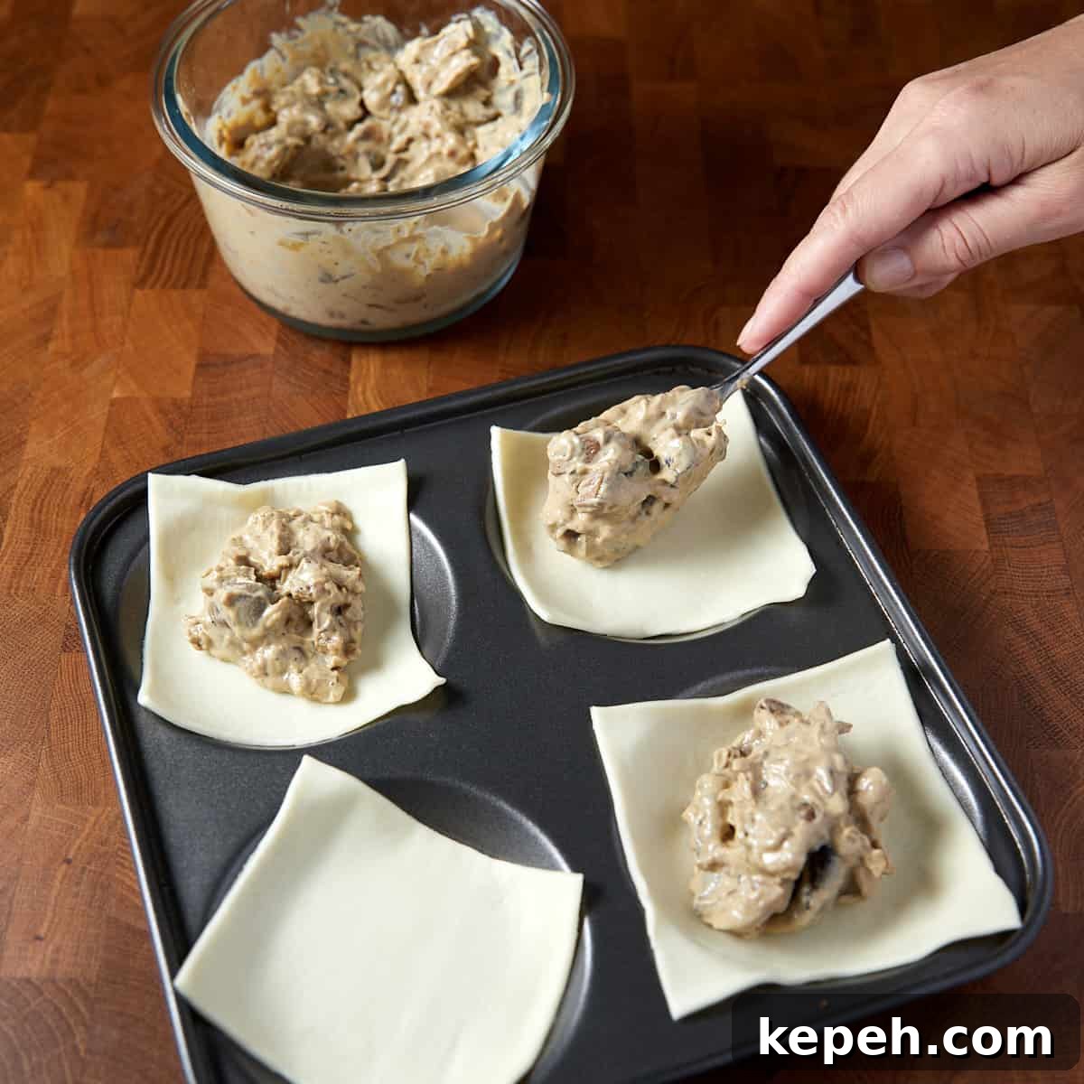 Photo showing the squares of pastry and a dollop of cooled mushroom filling mixture being put into the middle of each.