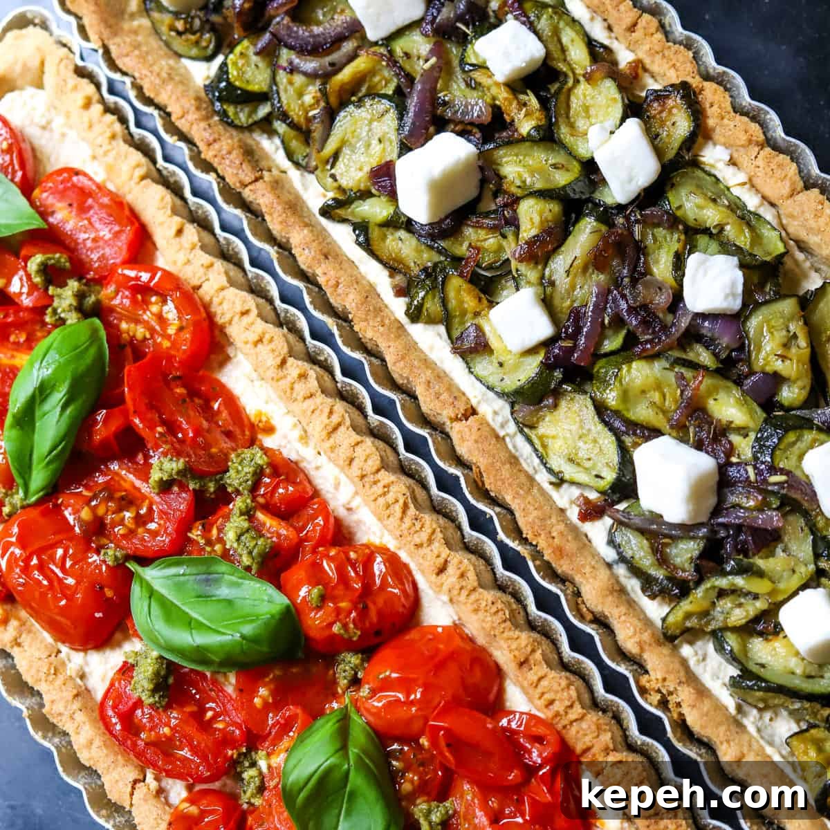Photo of rectangular vegan roasted vegetable tarts together, one topped with courgette (zucchini) and red onion, the other with tomatoes and pesto.