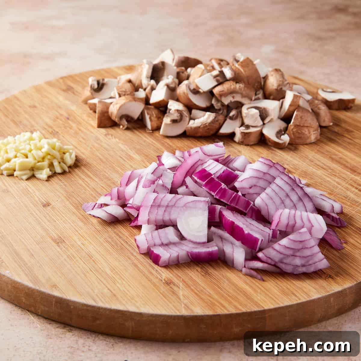 Photo showing the chopping size for the mushrooms, red onion and garlic, all set in piles on the chopping board.