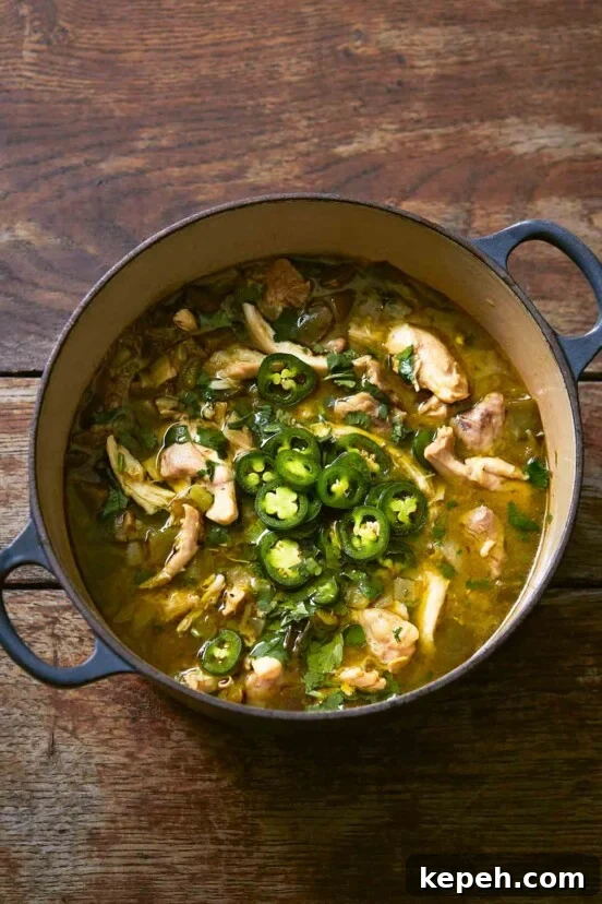 A large blue Dutch oven filled with green chicken chili, topped with sliced jalapenos.