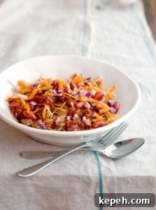 A white bowl of turkey Cincinnati chili with a fork and spoon resting beside it.