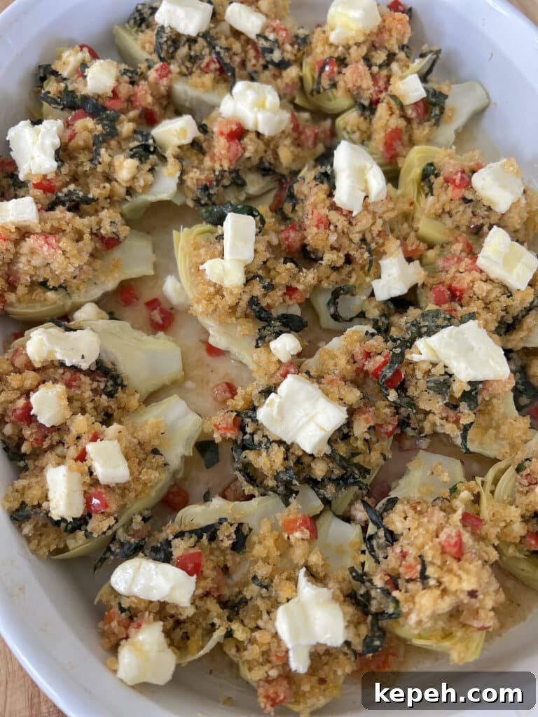 Breadrumb topped artichoke heart halves topped with small cubes of butter in white baking dish.