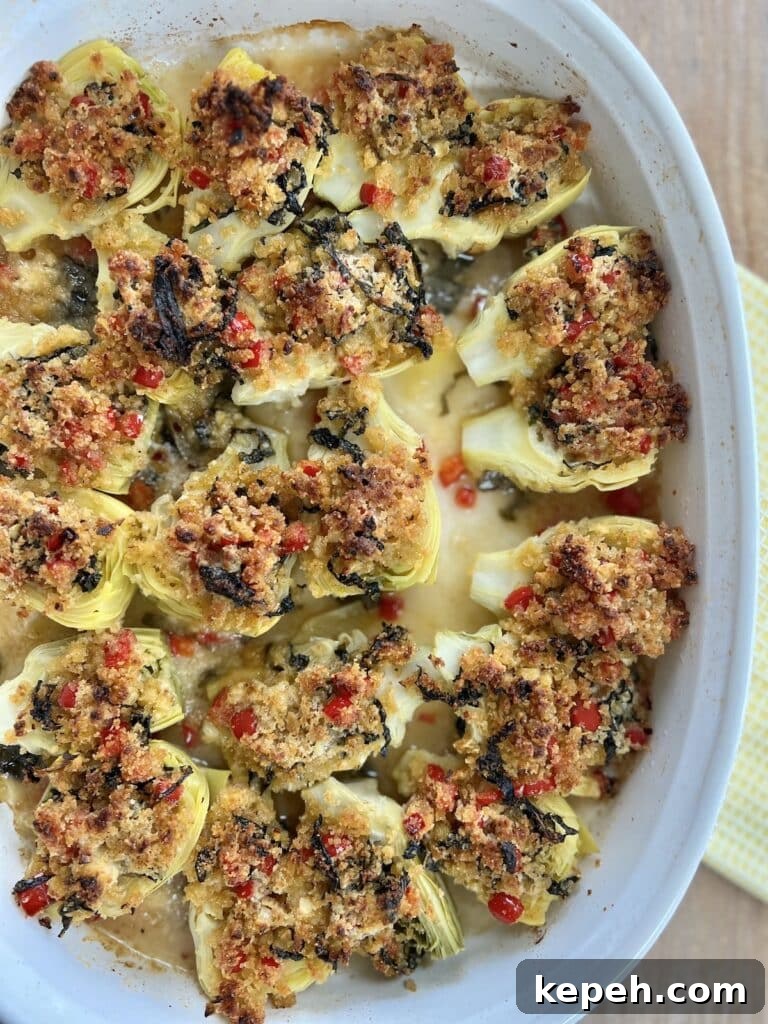 Finished, baked italian artichoke hearts oreganata in white baking dish on yellow towel.