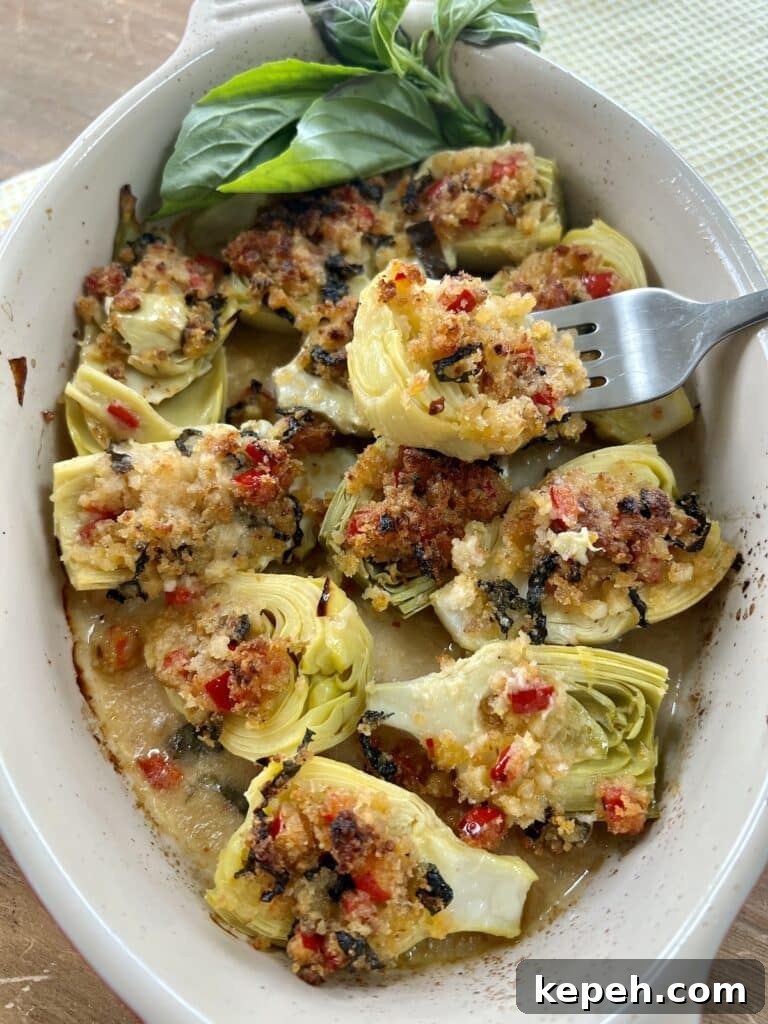 Piece of roasted Italian artichoke hearts oreganata with lemon basil breadcrumbs on fork over baking dish full of them with basil garnish.