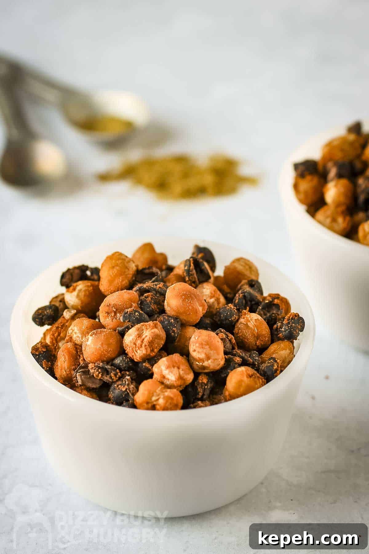 Side shot of two white bowls of chickpeas and black beans with spices and measuring cups in the background.