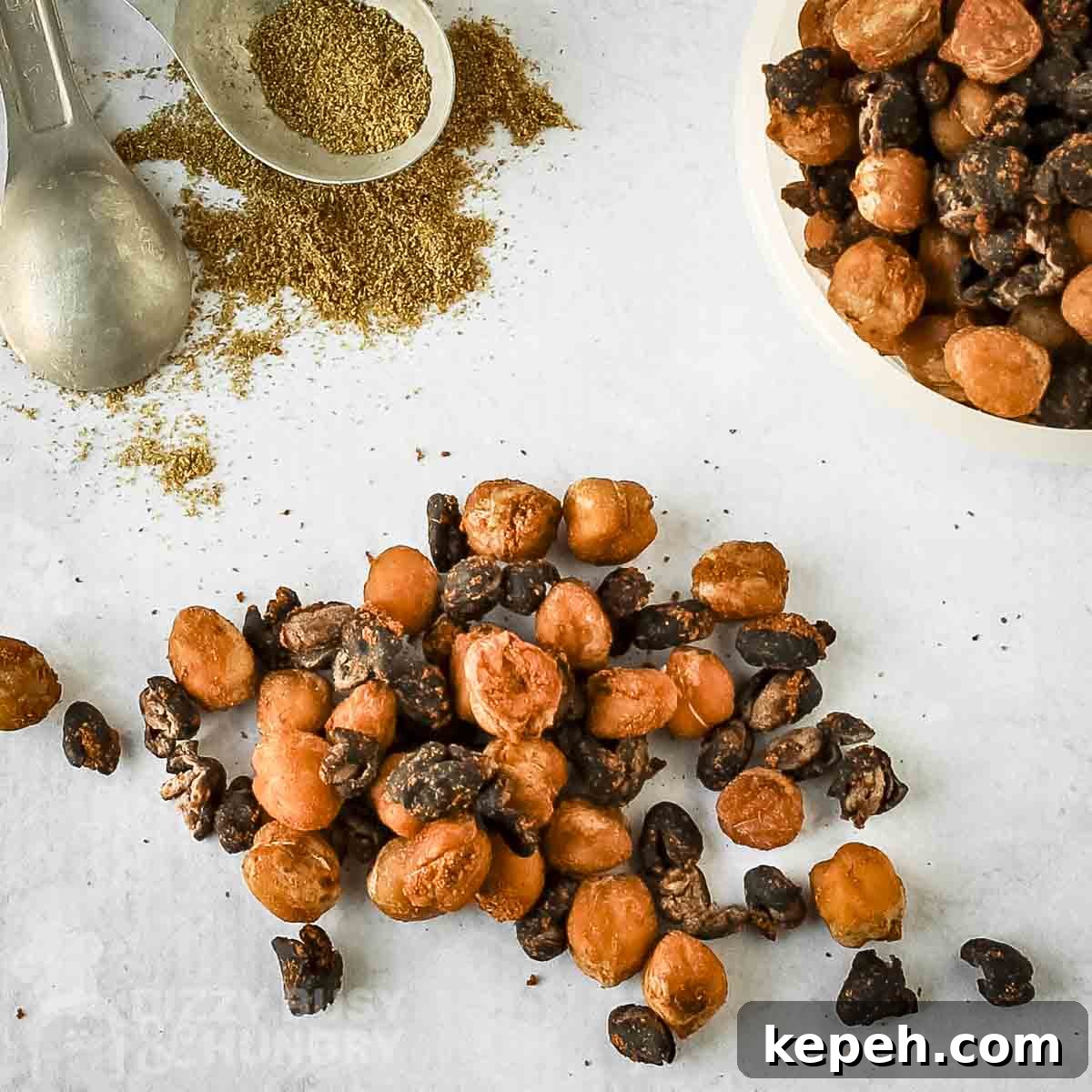 Close up overhead shot of roasted chickpeas and black beans on a white surface with spices in the background.
