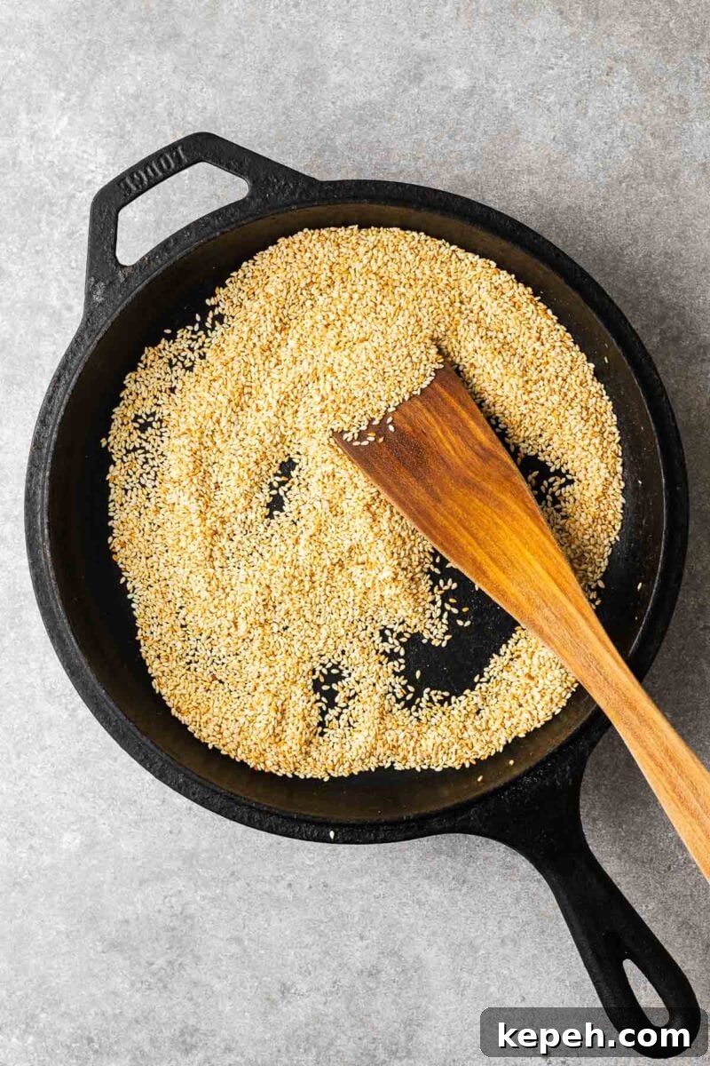 How to Toast Sesame Seeds on the Stove or in the Oven 8 Toasted sesame seeds in a skillet being stirred with a wooden spoon.