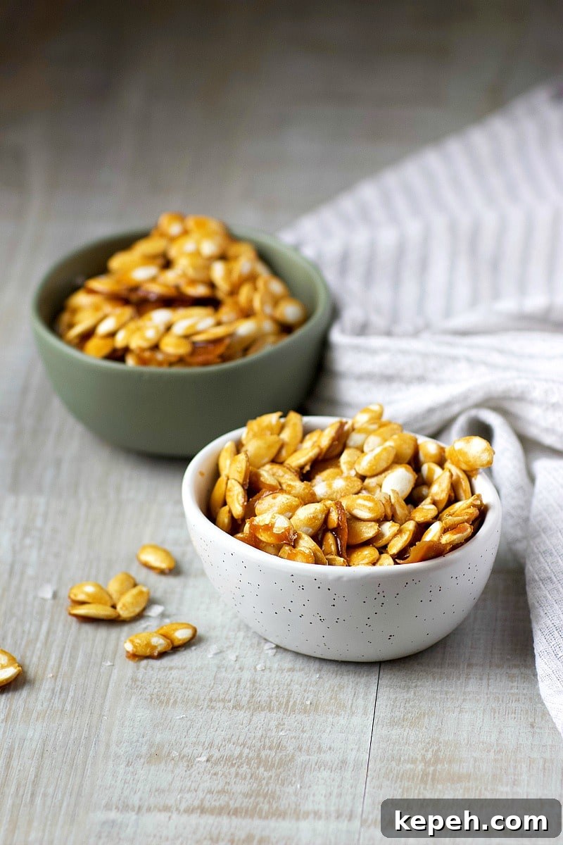 Salted Caramel Pumpkin Seeds Recipe — Crunchy Fall Snack 2 Salted Caramel Pumpkin Seeds in a green bowl and a white bowl on a grey and white tea towel.