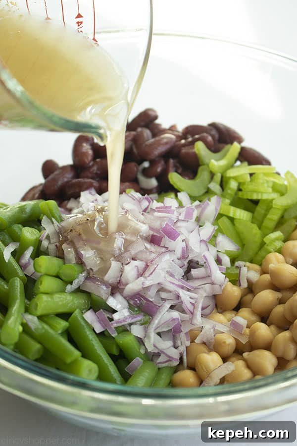 Classic Three-Bean Salad Recipe for Summer Potlucks 8 Dressing being poured from a measuring cup over bean salad ingredients