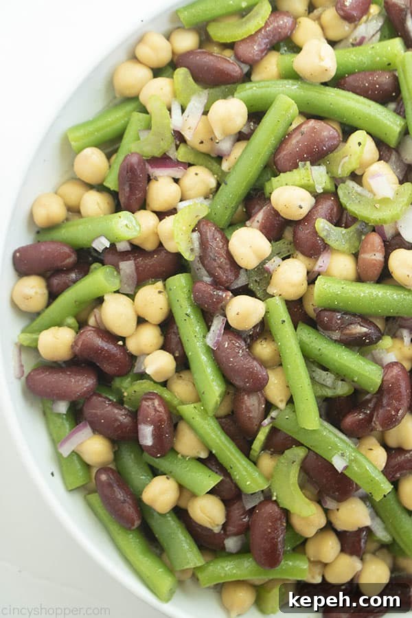 Classic Three-Bean Salad Recipe for Summer Potlucks 3 White bowl with a variety of beans, onions, celery, and spices