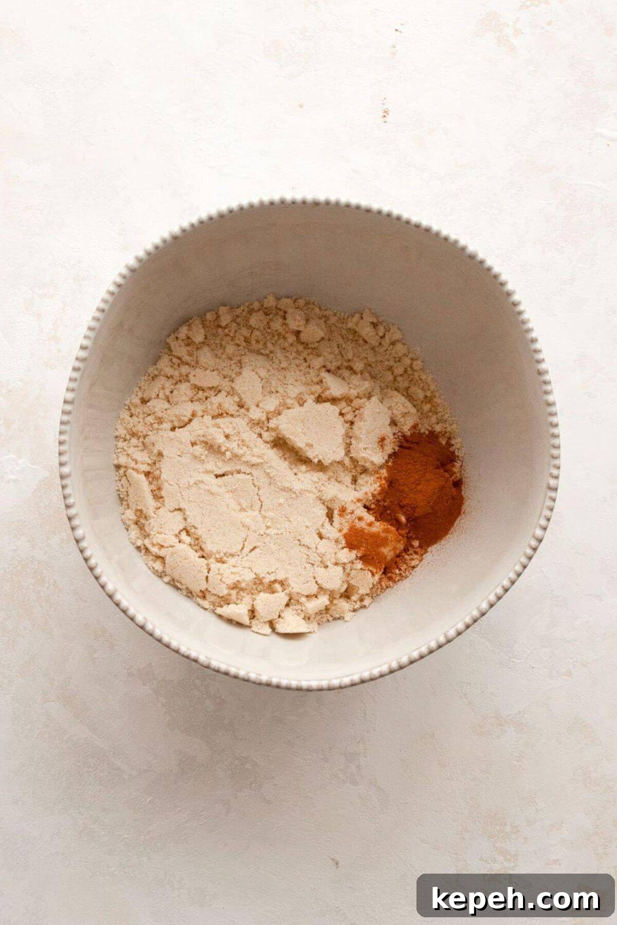 Whisking almond flour, oat flour, cinnamon, baking powder, and salt together in a white mixing bowl.