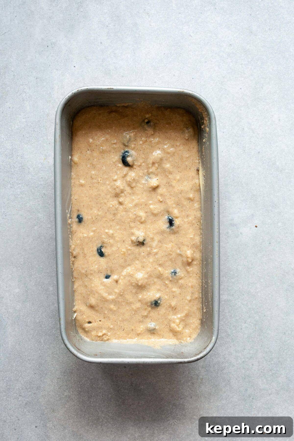 Fresh blueberries folded into banana bread batter with a spatula in a glass mixing bowl.