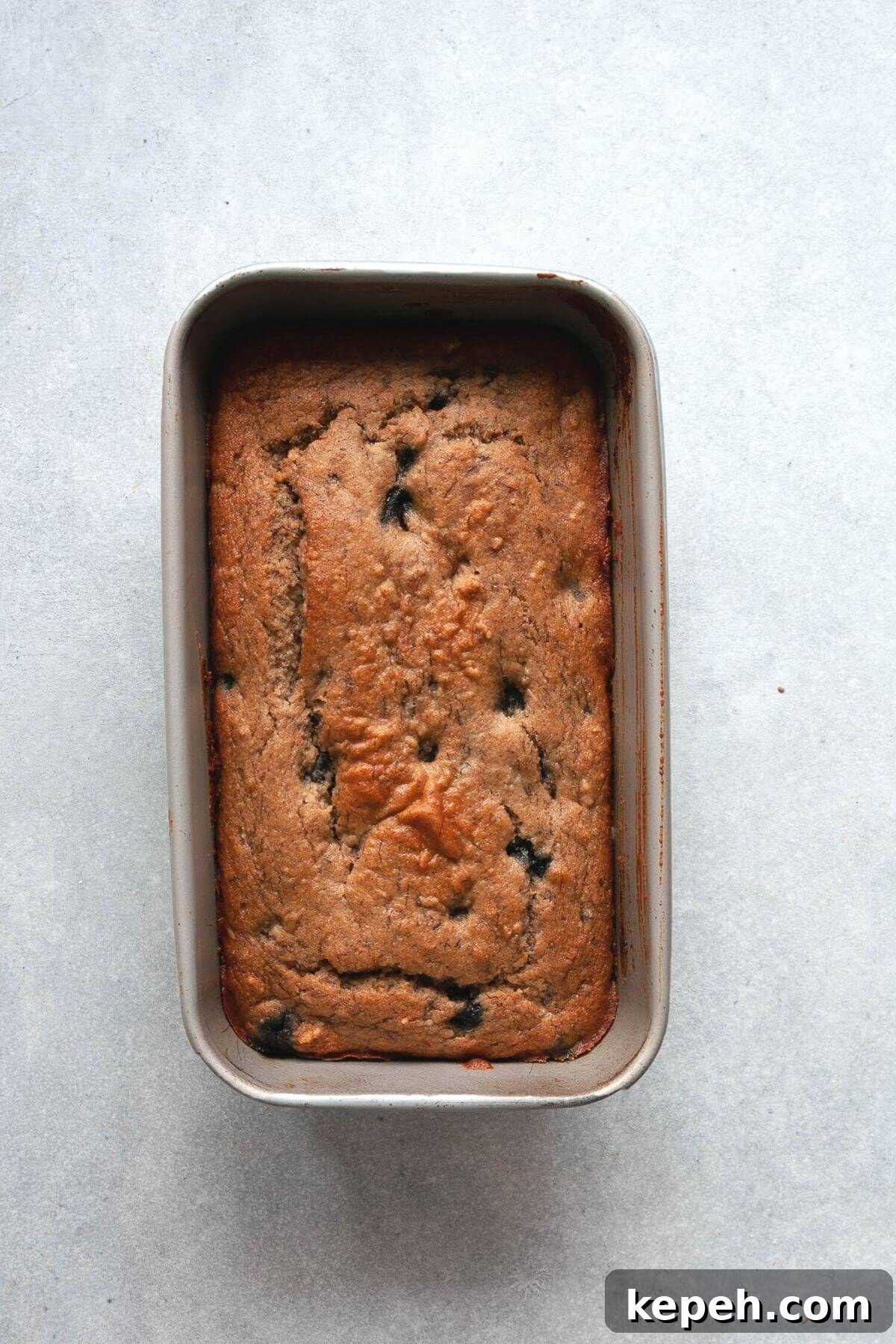 Golden-brown healthy blueberry banana bread fresh from the oven in a loaf pan.