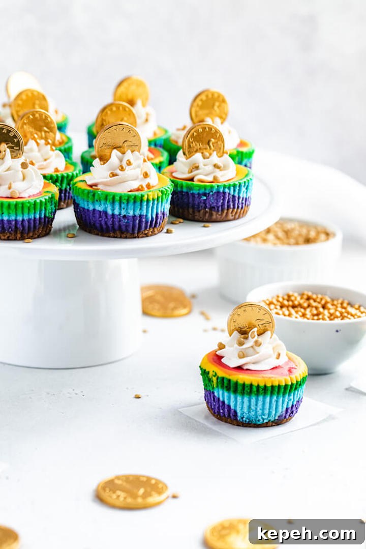 Mini Rainbow Cheesecakes with Pot of Gold Surprise 9 cheesecake cupcakes on a white cake stand