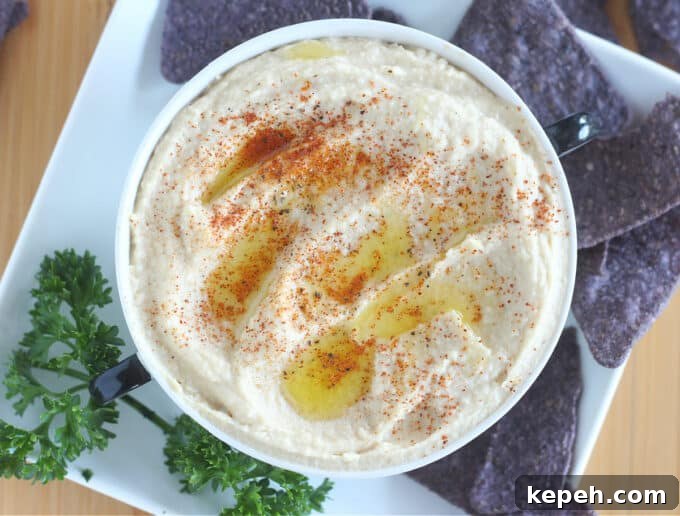 Top down view of hummus in a bowl surrounded by chips and parsley.