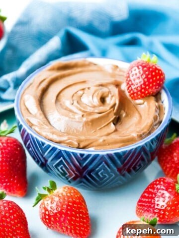 A blue bowl filled with a chocolate avocado mousse with a strawberry on top of it and strawberries around the bowl.