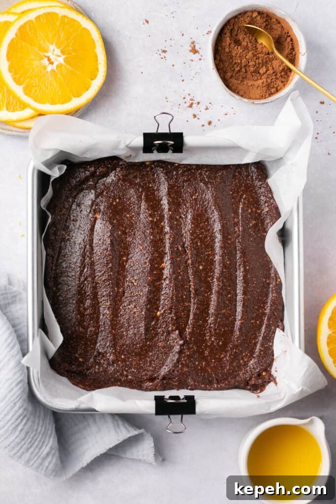 No-Bake Orange Chocolate Fudge Recipe: Zesty Cocoa Treat 6 A square baking pan lined with parchment paper with a chocolate mixture in it.