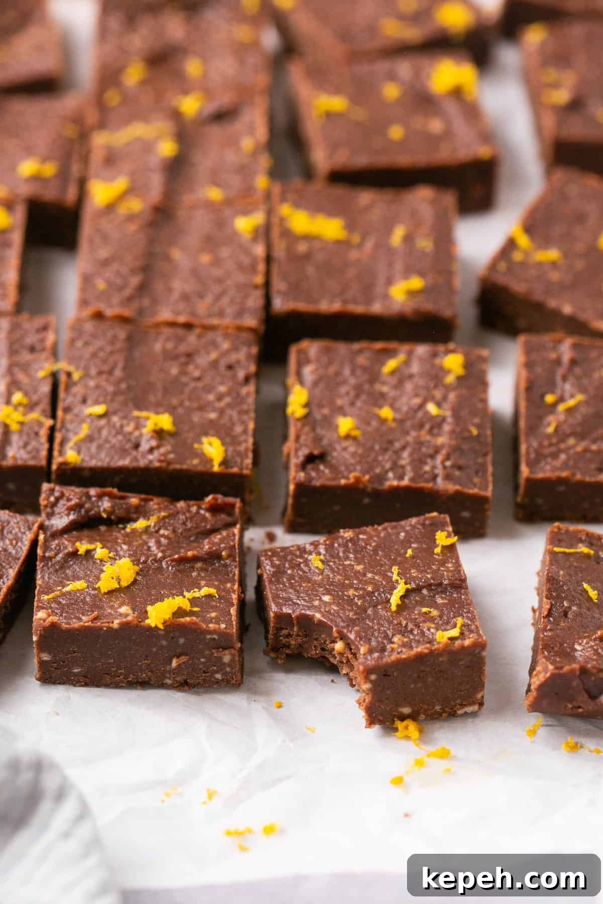 No-Bake Orange Chocolate Fudge Recipe: Zesty Cocoa Treat 9 Orange chocolate fudge pieces on parchment paper garnished with orange zest and one of the pieces has a bite out of it.