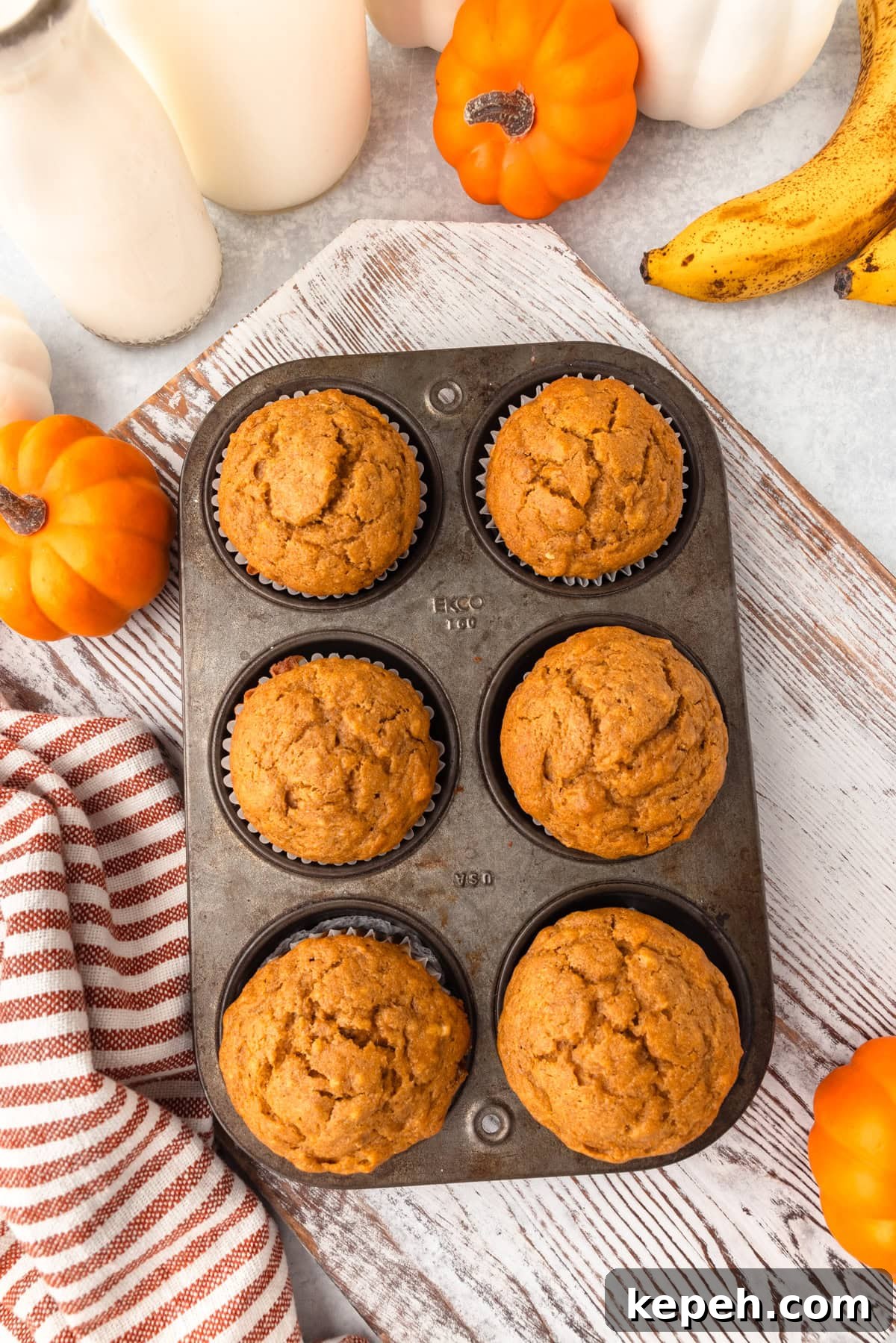 Cupcakes in a baking tin on a rustic wooden surface with pumpkins, bananas, and a striped cloth.