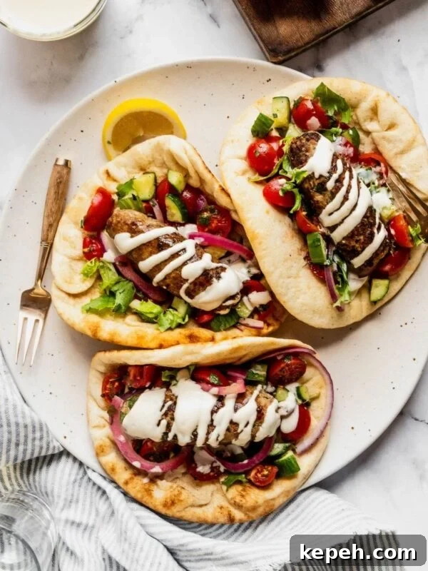Plate with three turkey kofta wraps garnished with tahini sauce, pickled onions and chopped salad with cherry tomatoes and cucumbers.