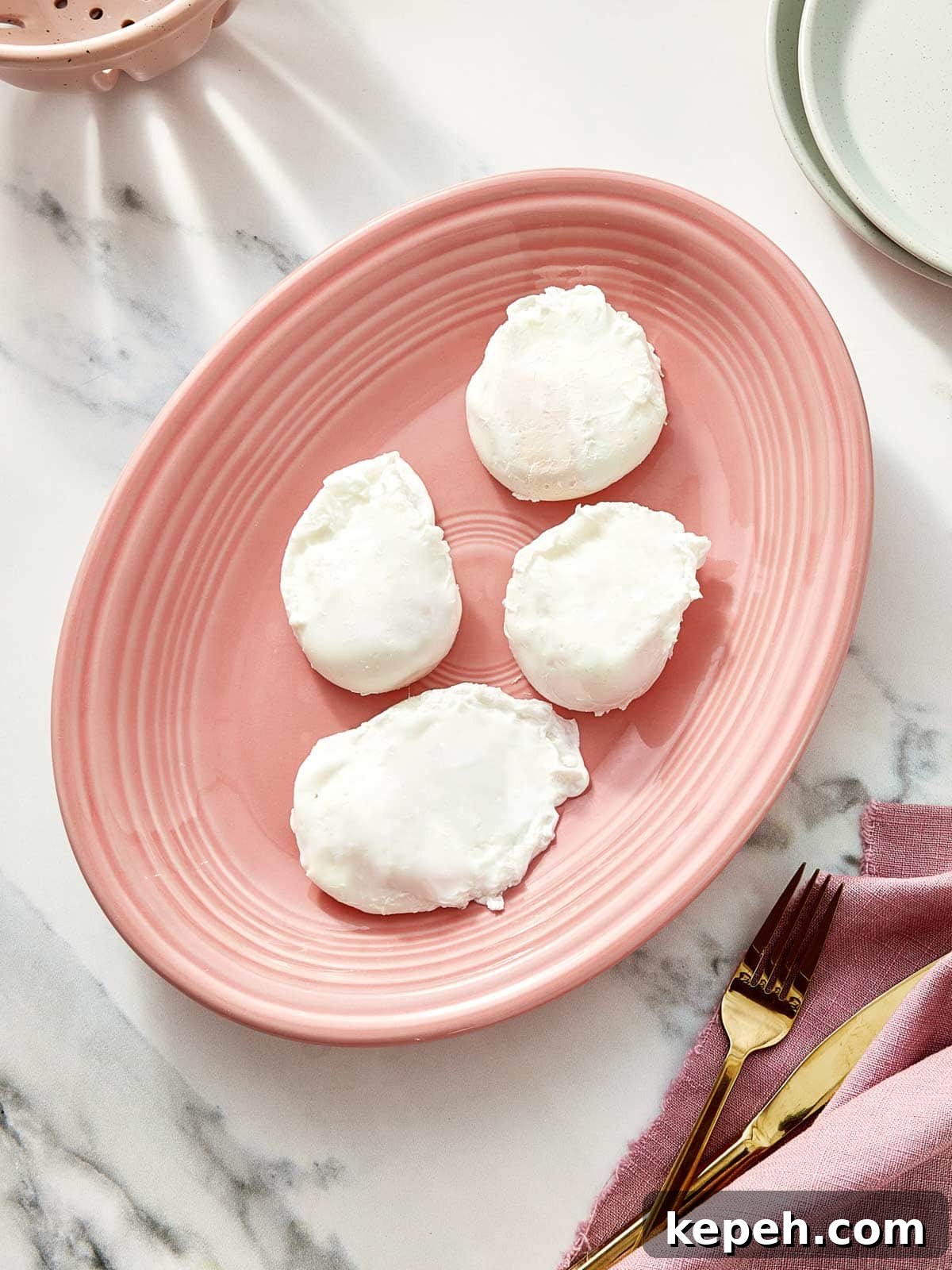 Four perfectly poached eggs resting on a blush-pink plate over a marble background.