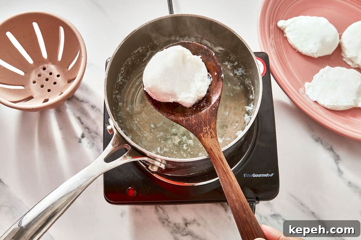 A poached egg being lifted from hot water with a slotted spoon, surrounded by perfectly cooked eggs on a plate.