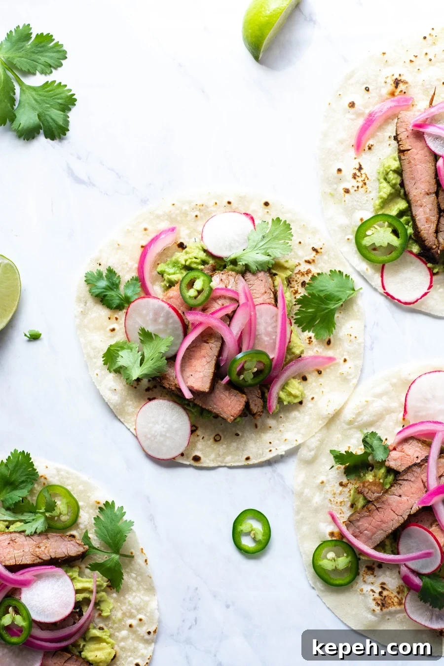Marinated Steak & Avocado Tacos (Gluten-Free) 2 Multiple steak tacos on a white background with cilantro, thinly sliced jalapeno, pickled red onions