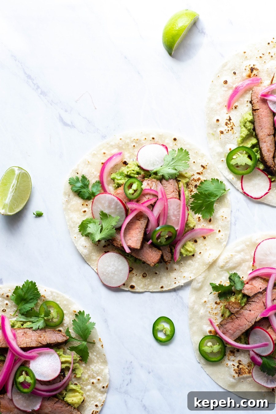 Marinated Steak & Avocado Tacos (Gluten-Free) 6 Multiple steak tacos on a white background with cilantro, thinly sliced jalapeno, pickled red onions