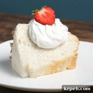 Light and Fluffy Angel Food Cake Recipe for Perfect Desserts 5 A slice of angel food cake topped with a dollop of whipped cream and a halved strawberry sits on a white plate, set against a wooden table and blue background.