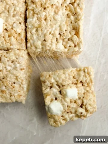 a close up of brown butter rice krispie treats with a marshmallow being pulled and stretched.