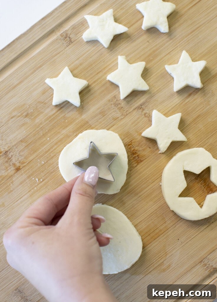 A hand uses a star-shaped cookie cutter to cut star shapes from mozzarella slices on a wooden board.