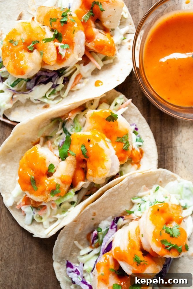 Crispy Bang Bang Shrimp Tacos with Creamy Slaw 2 A wooden board topped with three bang bang shrimp tacos next to a bowl of bang bang sauce.