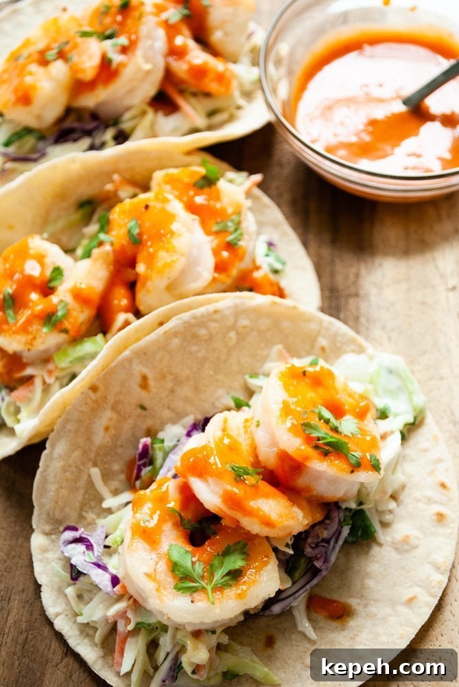 Crispy Bang Bang Shrimp Tacos with Creamy Slaw 3 Three bang bang shrimp tacos on a wooden serving board next to a bowl of bang bang sauce.