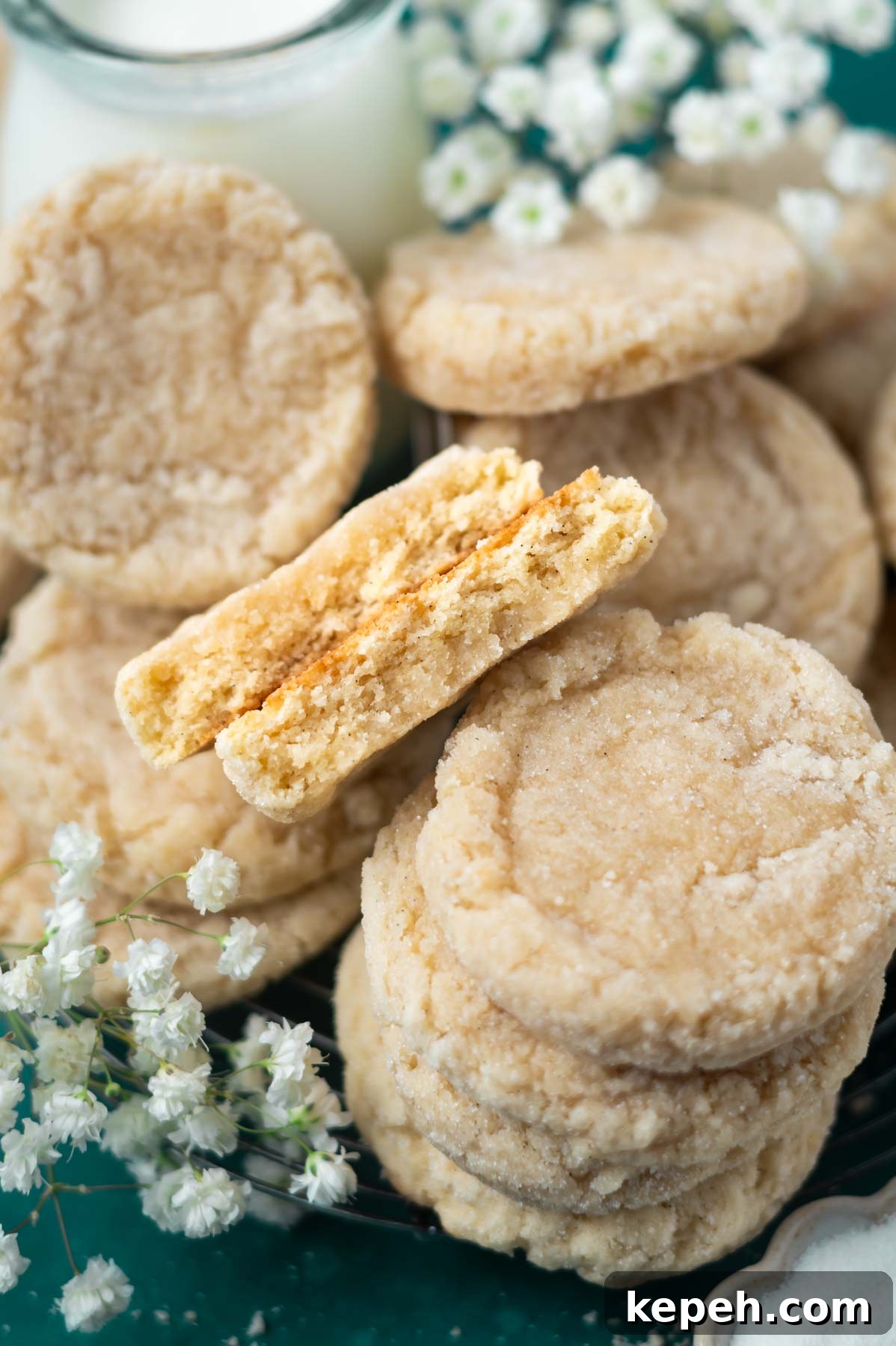 Classic Vanilla Bean Cookies with Old Fashioned Flavor 3 broken cookie, showing thick and soft texture, nestled among stacks of cookies with a glass of milk and fresh flowers