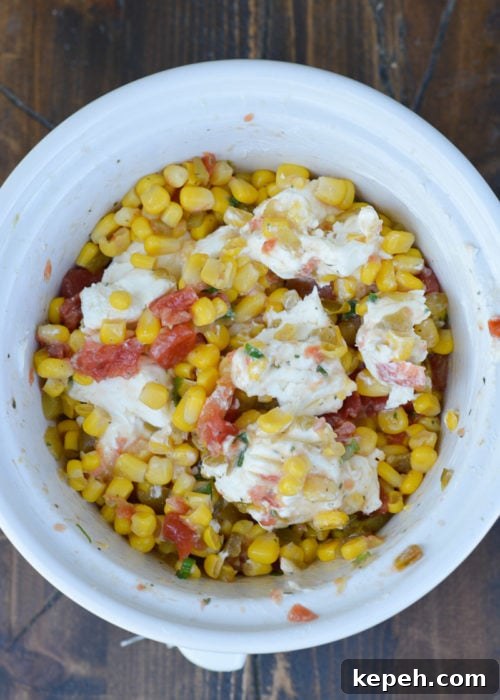 Creamy Slow Cooker Corn Dip 6 softened cream cheese stirred into the corn, tomato, green chili, ranch seasoning, and chopped green onions in a white slow cooker.