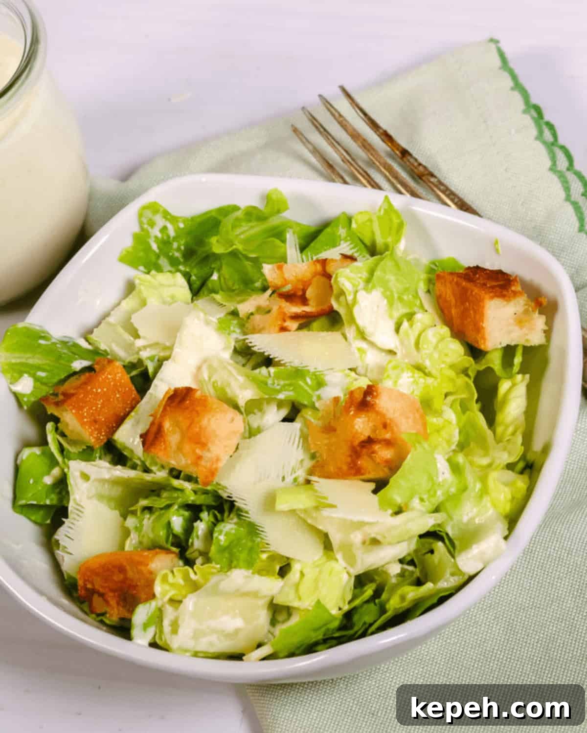 Classic Caesar Salad with Homemade Dressing 3 Bowl of the best Caesar salad with croutons and shaved parmesan cheese, accompanied by a fork and dressing on the side.