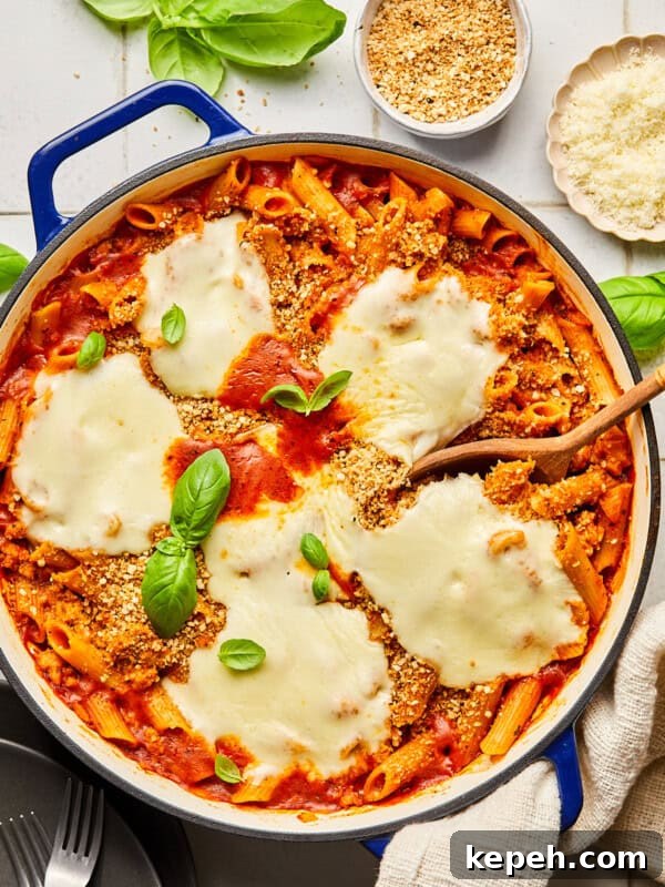 chicken parmesan pasta in a blue dutch oven surrounded by basil and ingredients