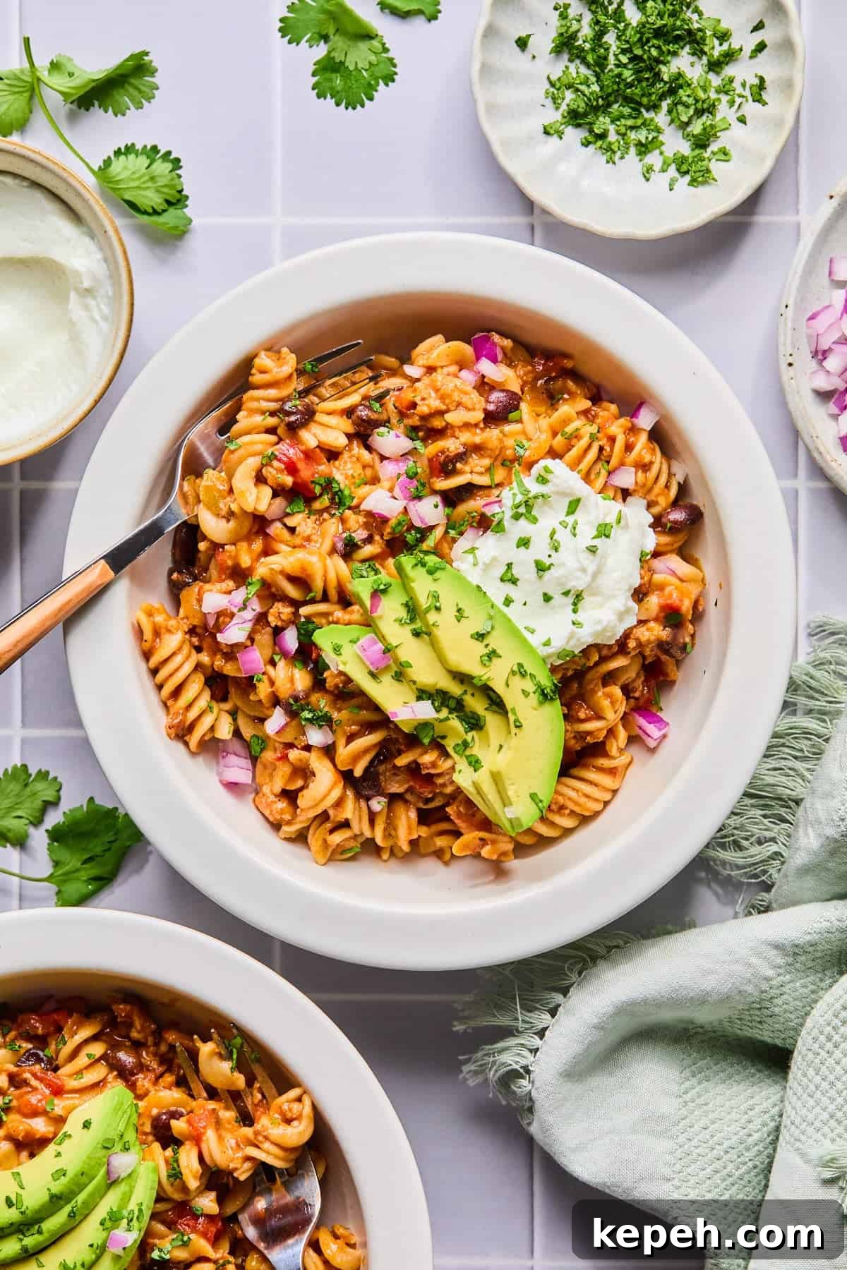 Bowl of one pot taco pasta garnished with sour cream, avocado, and cilantro with a fork.
