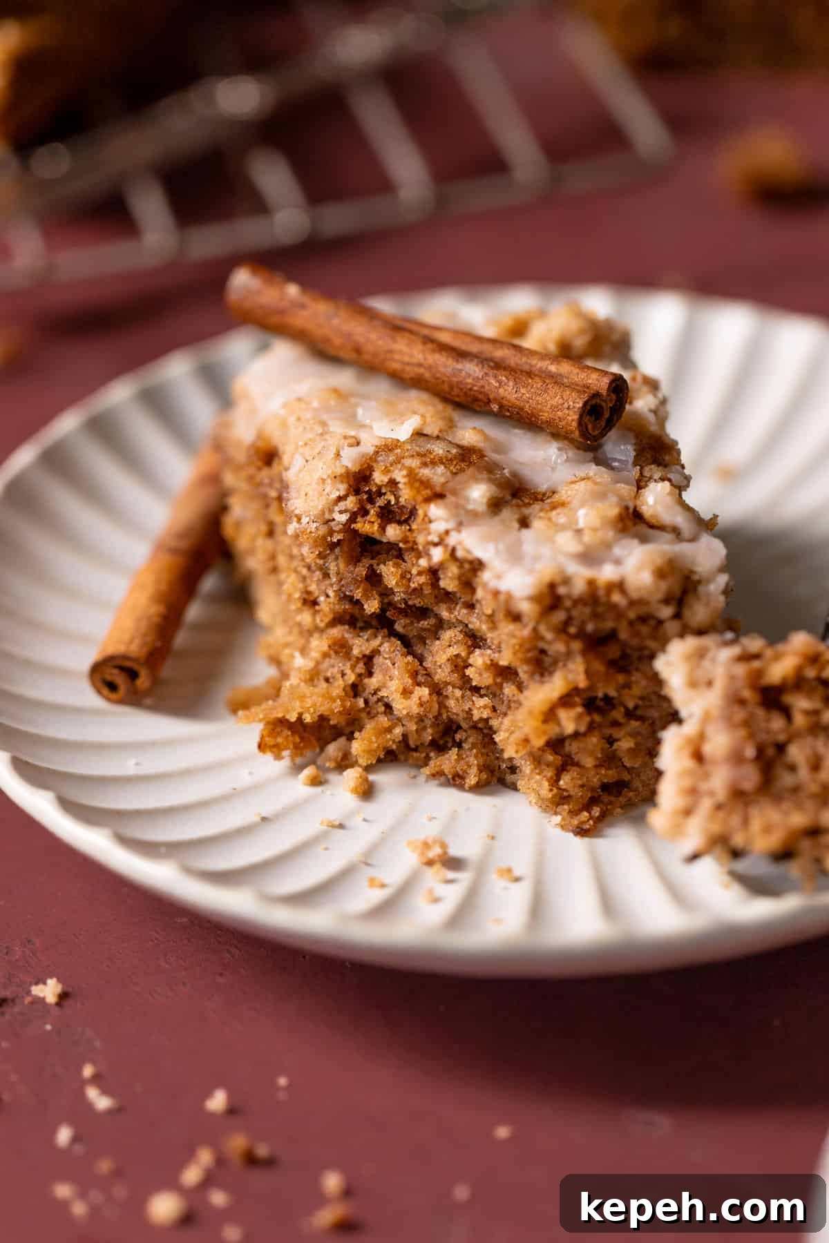 A slice of apple cake on a plate with a stick of cinnamon on top.