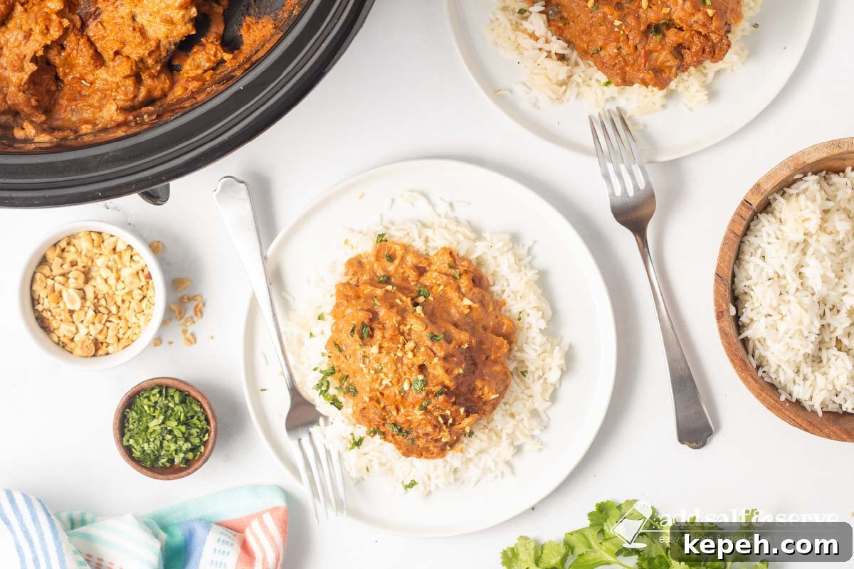 Slow Cooker Thai Peanut Chicken Recipe 8 Plated slow cooker Thai Peanut Chicken over rice garnished with chopped peanuts and cilantro.