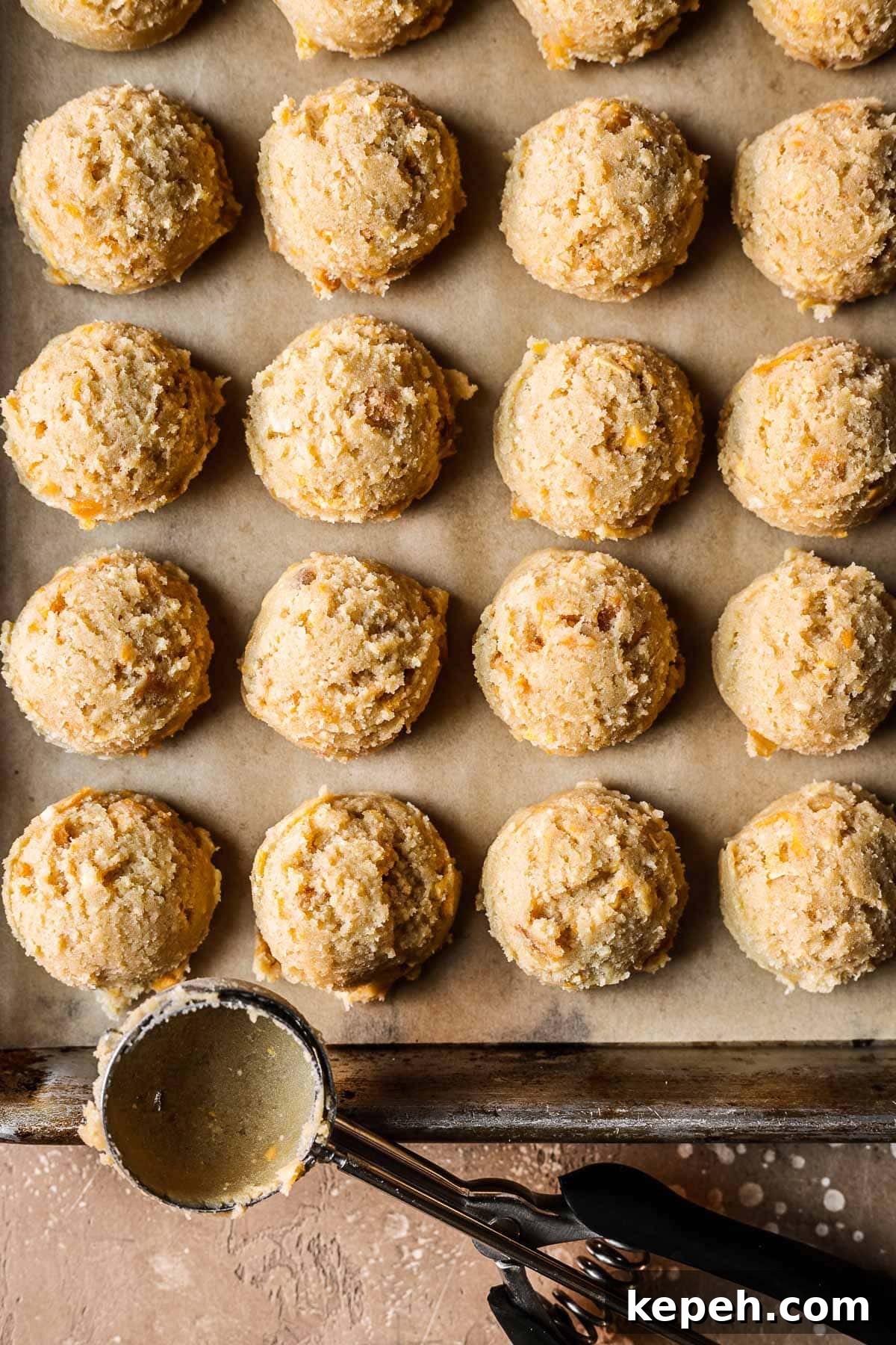 Scoops of mango cookie dough on a parchment lined baking sheet.