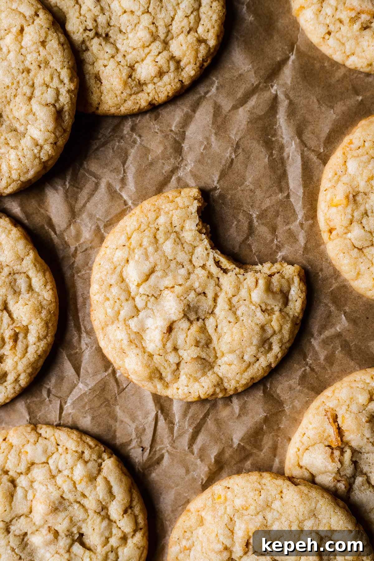 A cookie on brown parchmenet with one bite taken out of it. More cookies peek into the frame.