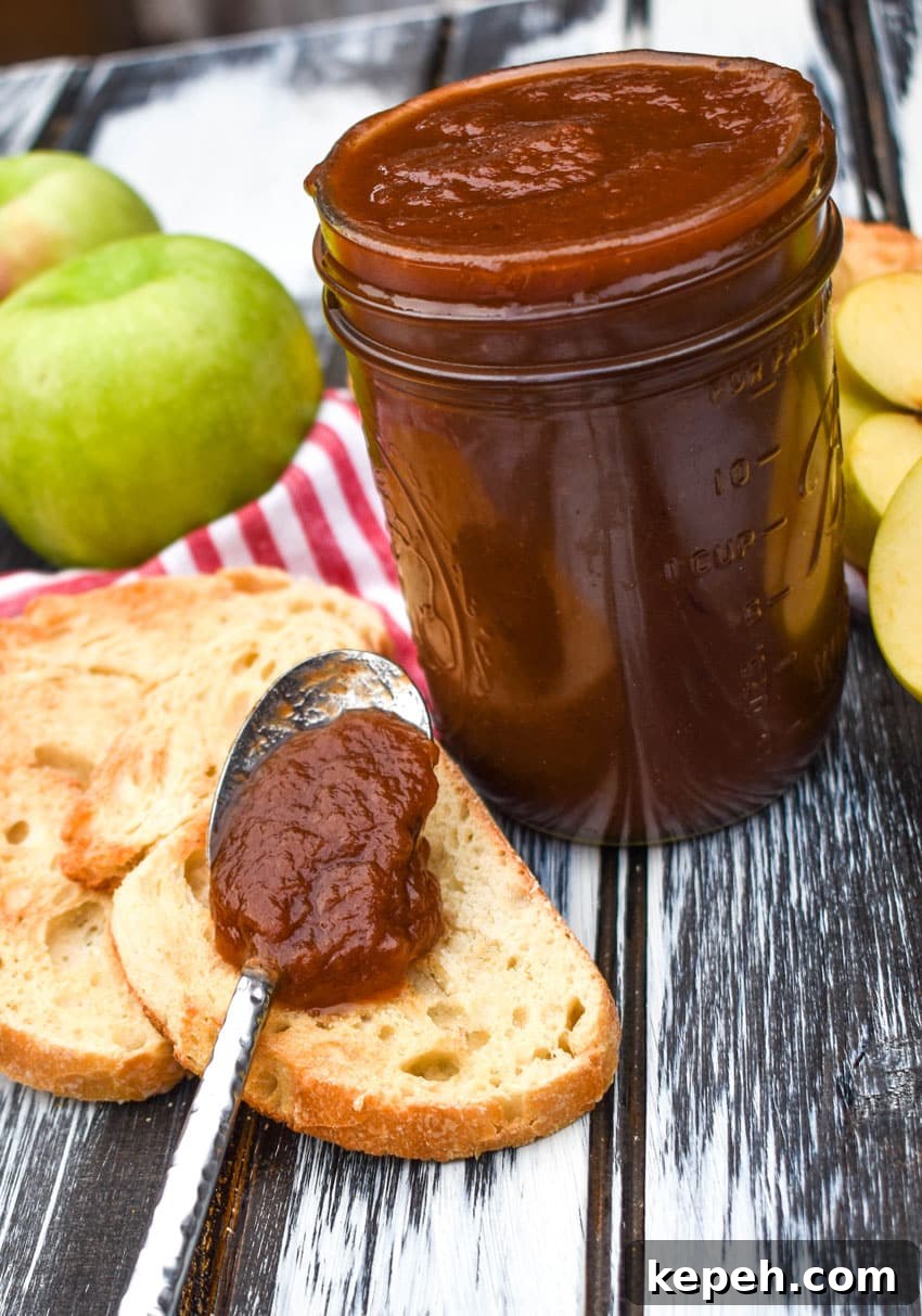 a spoon filled with crockpot apple butter resting on a slice of toasted baguette