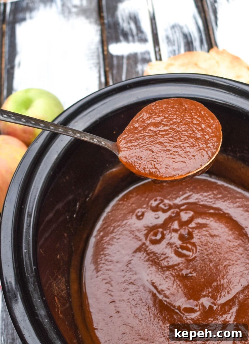 a silver ladle scooping homemade apple butter out of a black crockpot