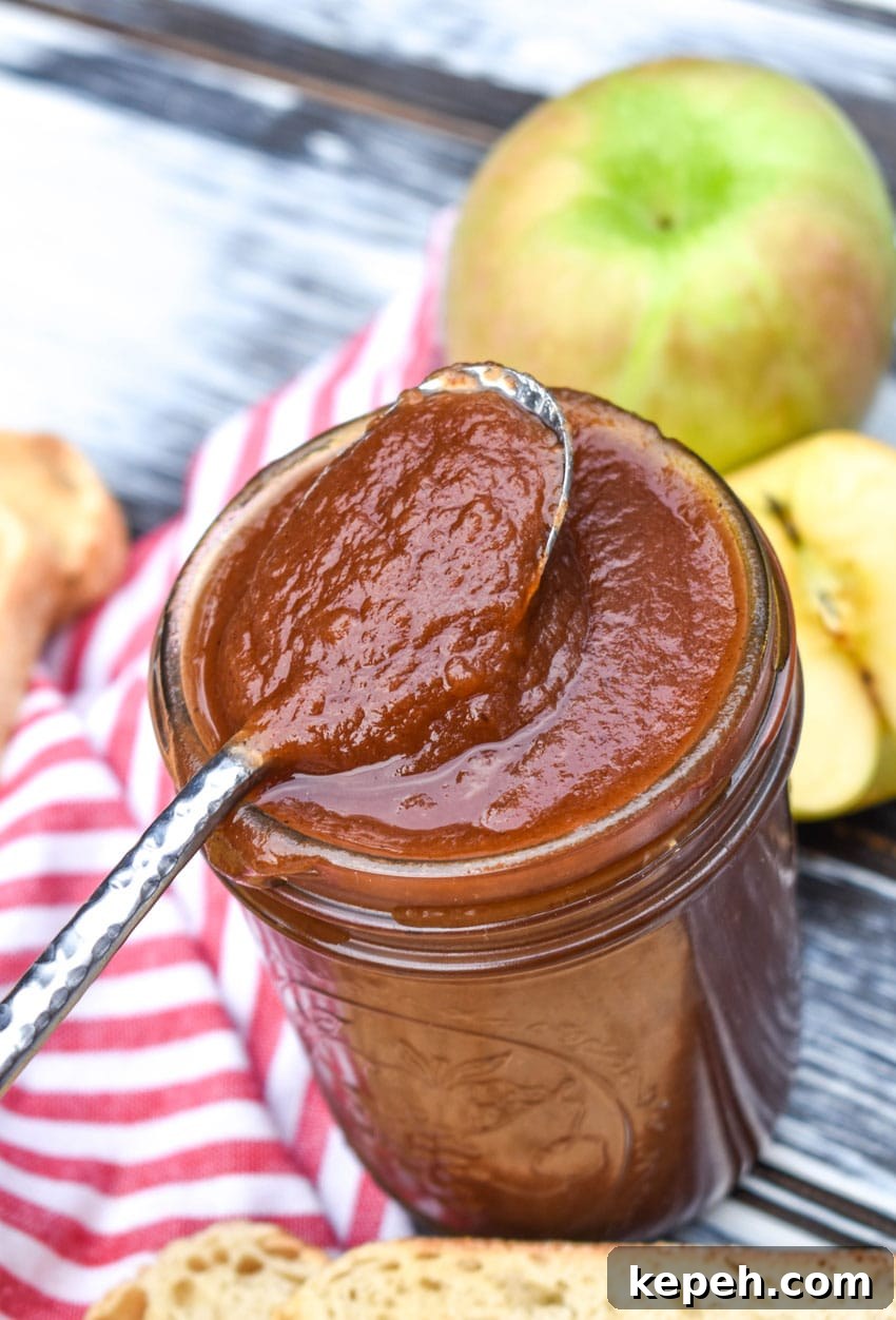 a silver spoon resting on the edge of a glass jar filled with easy crockpot apple butter