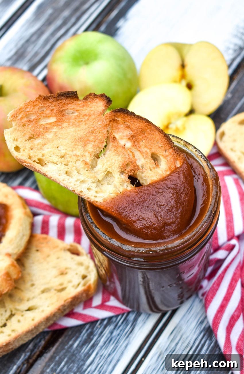 a slice of toast being dipped in a glass jar filled with crockpot apple butter