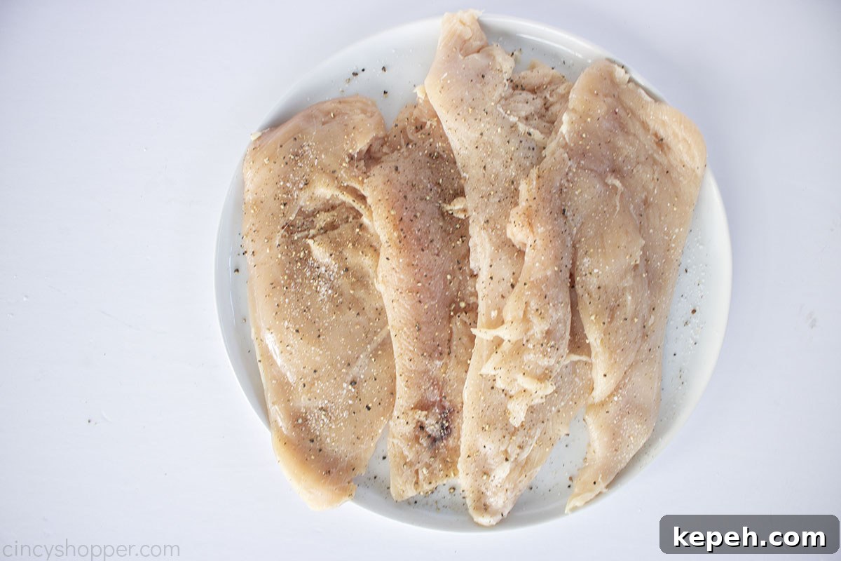 Raw chicken breasts butterflied and pounded with salt and pepper on a white plate.